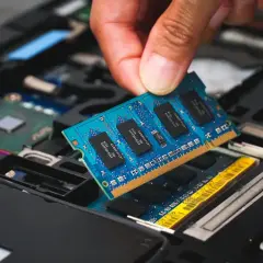 En hand sätter i ett blått ram dimm-kort i en öppen laptop.