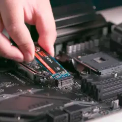 En hand monterar en M.2 NVMe SSD på ett moderkort. Detta är en snabb lagringslösning som kan förbättra datorns prestanda avsevärt.