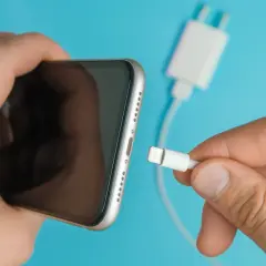 En hand försöker koppla in en laddningskabel i en iPhone, men den laddar inte.