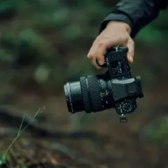 En hand håller en Fujifilm GFX 50S II med ett objektiv i en regnig skogsmiljö.