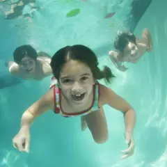 Barn simmar glatt under vattnet i en pool. Det är som att filma under vatten med dessa glada ansikten.