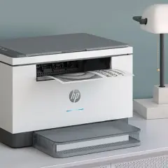 En vit och grå HP-skrivare, den minsta laserskrivaren, skriver ut ett dokument. Bredvid står en lampa med marmorbas.