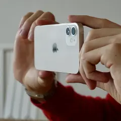 Händerna håller en vit iPhone 15 med dubbla linser på kameran, redo att ta en bild.