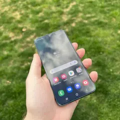 En hand håller en Samsung-telefon med aviseringar på skärmen, med gräs i bakgrunden.