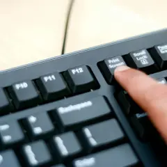 En finger trycker på "Print Screen"-tangenten på ett tangentbord. Så här tar man screenshot på datorn.
