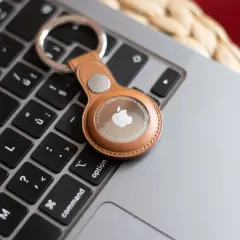 En brun läderfodral med en Apple AirTag ligger på ett tangentbord. Även om AirTag är designad för iPhone, kan den användas med Android-enheter via webben.