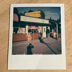 En polaroidkamera bild av en pizzeria och kiosk med en glasskylt. En person går in genom dörren.