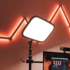 En stor, ljusstark key light lyser upp scenen. Bakom den syns en datorskärm med Stream Deck-mjukvara och en webbkamera. Väggen pryds av en geometrisk ljusslinga i orange.