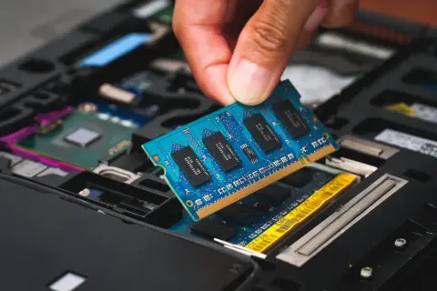 En hand sätter i ett blått ram dimm-kort i en öppen laptop.