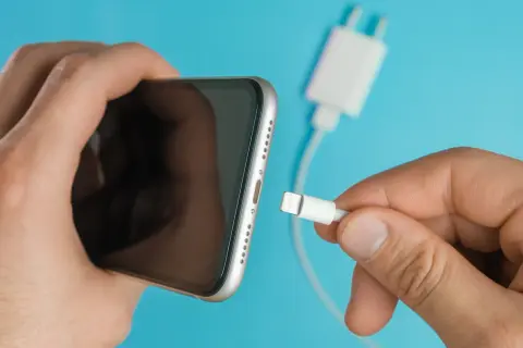 En hand försöker koppla in en laddningskabel i en iPhone, men den laddar inte.