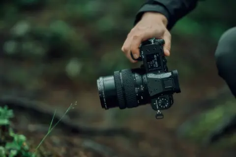 En hand håller en Fujifilm GFX 50S II med ett objektiv i en regnig skogsmiljö.
