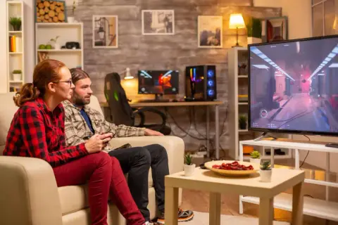 Ett par spelar tv-spel på en stor skärm, en bekväm casta från dator till tv-upplevelse.