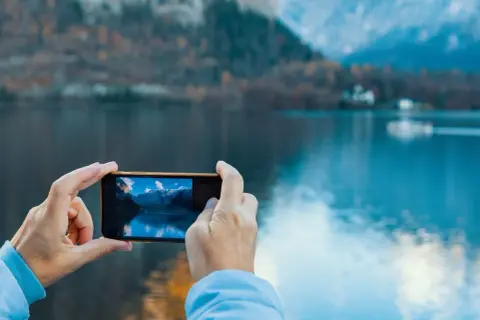 En selfie bild där en person tar foto av en vacker sjö och berg med sin mobil.