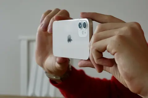Händerna håller en vit iPhone 15 med dubbla linser på kameran, redo att ta en bild.
