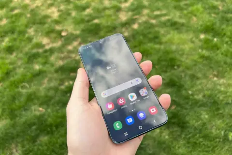 En hand håller en Samsung-telefon med aviseringar på skärmen, med gräs i bakgrunden.