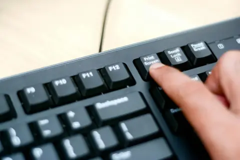 En finger trycker på "Print Screen"-tangenten på ett tangentbord. Så här tar man screenshot på datorn.