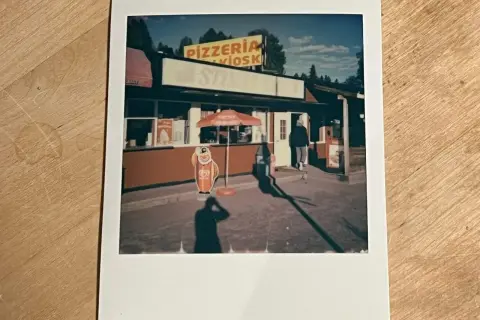 En polaroidkamera bild av en pizzeria och kiosk med en glasskylt. En person går in genom dörren.