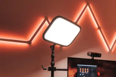 En stor, ljusstark key light lyser upp scenen. Bakom den syns en datorskärm med Stream Deck-mjukvara och en webbkamera. Väggen pryds av en geometrisk ljusslinga i orange.