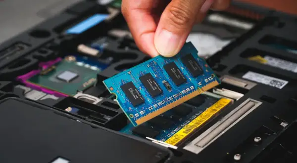 En hand sätter i ett blått ram dimm-kort i en öppen laptop.