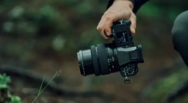 En hand håller en Fujifilm GFX 50S II med ett objektiv i en regnig skogsmiljö.