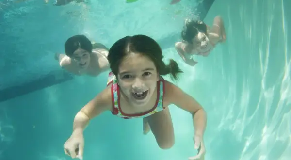 Barn simmar glatt under vattnet i en pool. Det är som att filma under vatten med dessa glada ansikten.