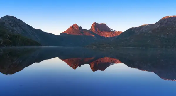 Bergstoppar i solnedgången speglas i en lugn sjö. En vacker vy som en samling av reels med bilder.