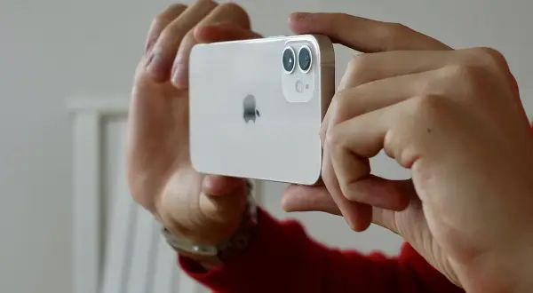 Händerna håller en vit iPhone 15 med dubbla linser på kameran, redo att ta en bild.