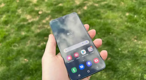 En hand håller en Samsung-telefon med aviseringar på skärmen, med gräs i bakgrunden.