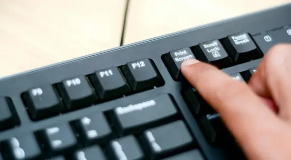 En finger trycker på "Print Screen"-tangenten på ett tangentbord. Så här tar man screenshot på datorn.