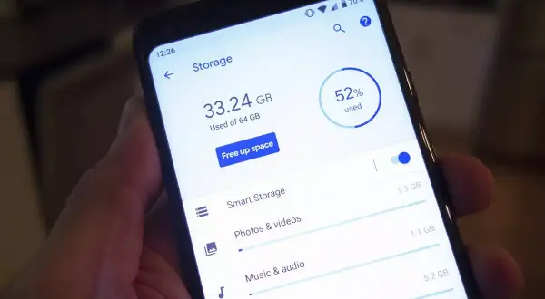 En hand håller en telefon som visar lagringsutrymme. 33.24 GB av 64 GB används, 52% totalt.