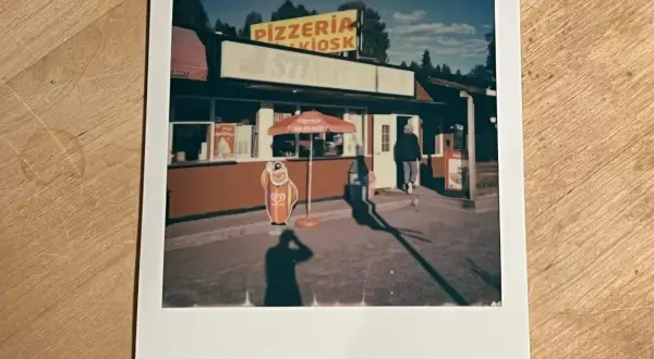 En polaroidkamera bild av en pizzeria och kiosk med en glasskylt. En person går in genom dörren.