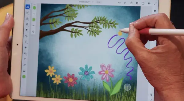 Handen skapar en magisk virvel med en penna i Adobe Fresco, över en bild av en drömsk äng med blommor och träd.