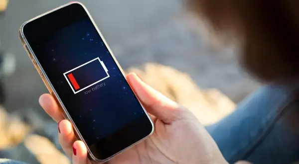 En person håller en mobil med lågt batteri. Dags att uppdatera telefonen och hitta en laddare!