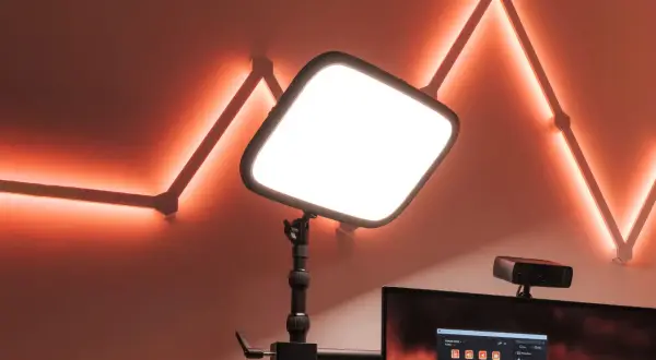 En stor, ljusstark key light lyser upp scenen. Bakom den syns en datorskärm med Stream Deck-mjukvara och en webbkamera. Väggen pryds av en geometrisk ljusslinga i orange.