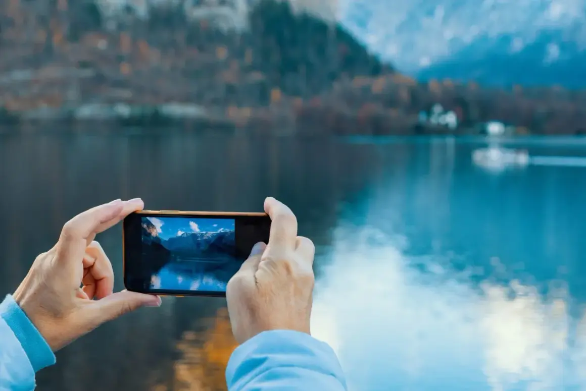 En selfie bild där en person tar foto av en vacker sjö och berg med sin mobil.