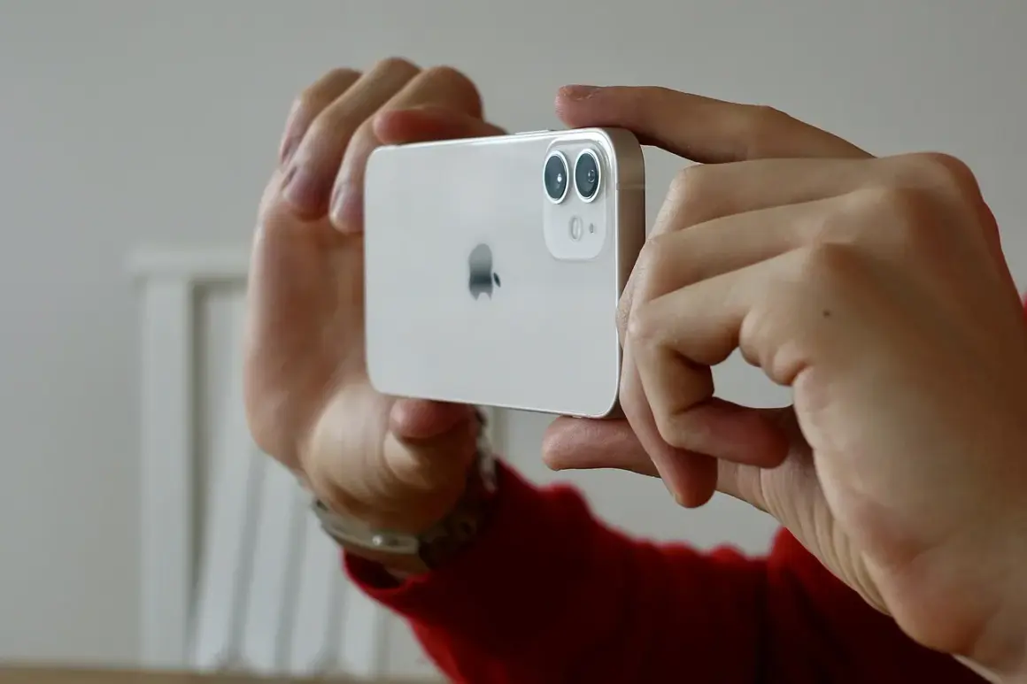 Händerna håller en vit iPhone 15 med dubbla linser på kameran, redo att ta en bild.