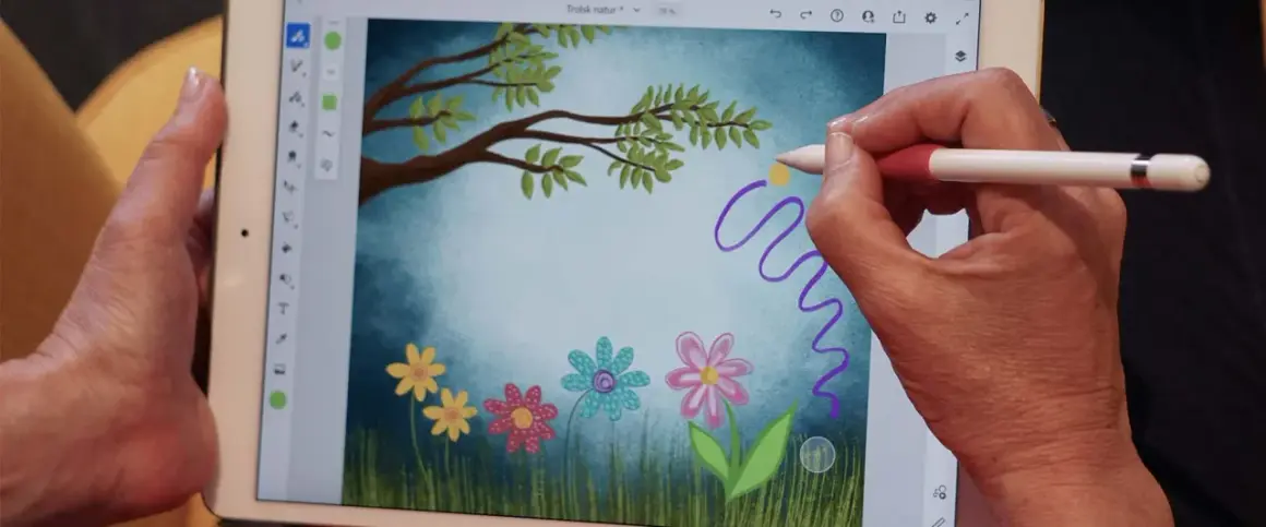 Handen skapar en magisk virvel med en penna i Adobe Fresco, över en bild av en drömsk äng med blommor och träd.