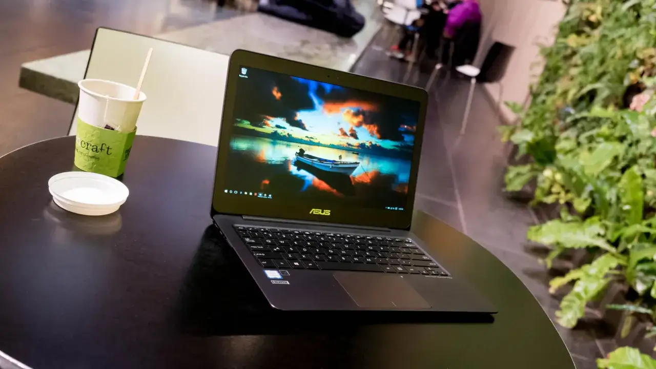 En Asus Zenbook UX305 st&aring;r p&aring; ett m&ouml;rkt bord bredvid en kopp med te och en gr&ouml;n v&auml;xtv&auml;gg.