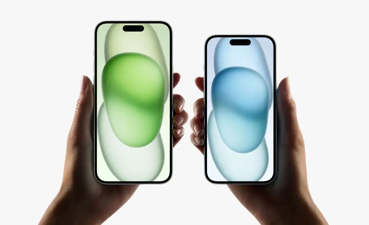 Två händer håller varsin iPhone 15 med en grön och en blå bakgrund.