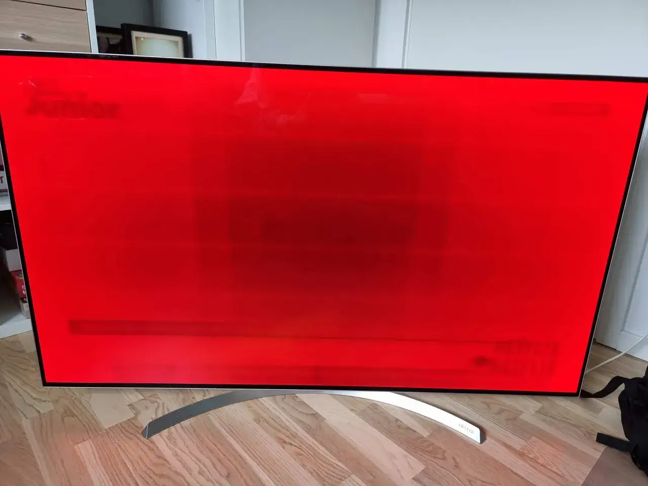 En r&ouml;d OLED-sk&auml;rm visar svaga sp&aring;r av text, troligen fr&aring;n tidigare visat inneh&aring;ll, vilket indikerar burn-in.