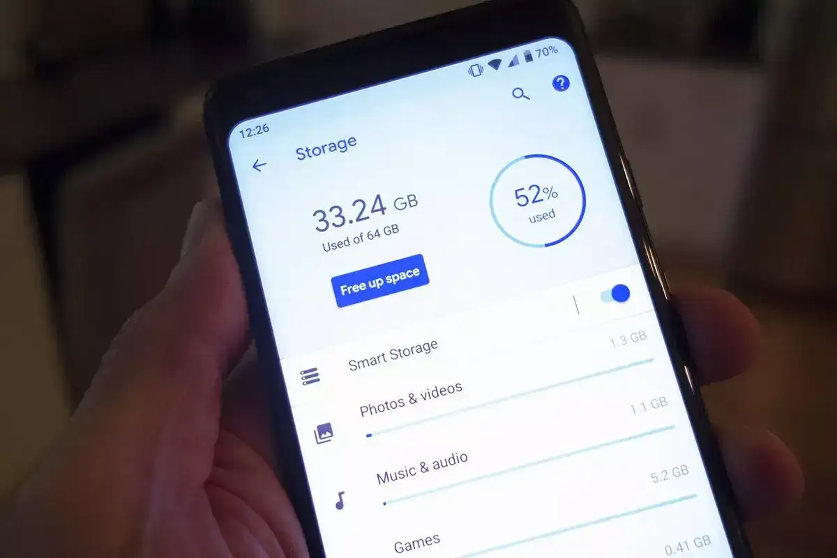 En hand håller en telefon som visar lagringsutrymme på en Samsung-enhet. 33.24 GB av 64 GB används, med 52% upptaget.