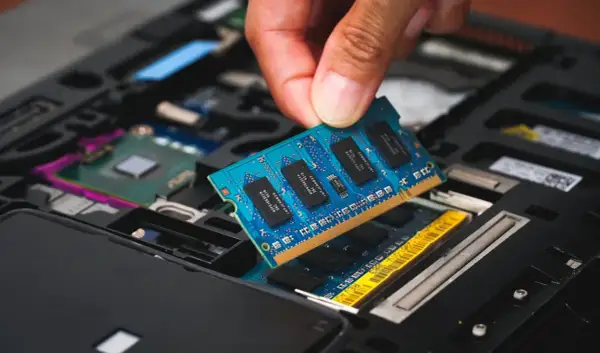 En hand sätter i ett blått ram dimm-kort i en öppen laptop.