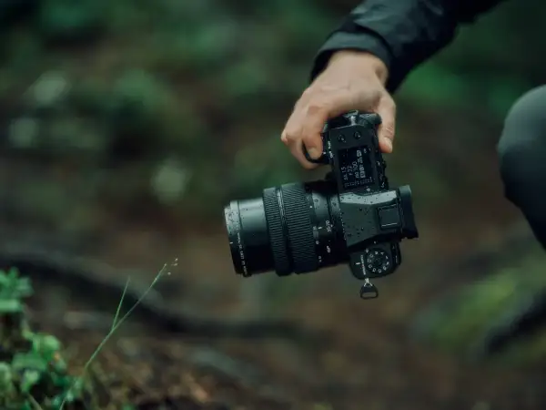 En hand håller en Fujifilm GFX 50S II med ett objektiv i en regnig skogsmiljö.