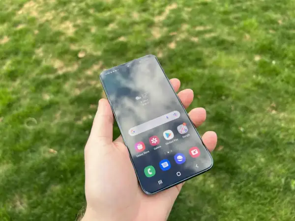 En hand håller en Samsung-telefon med aviseringar på skärmen, med gräs i bakgrunden.