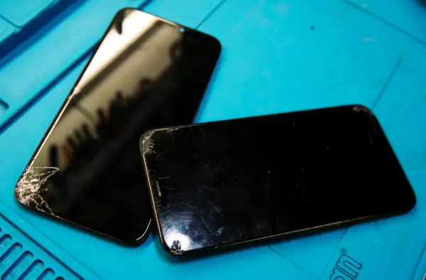 Två svarta mobiltelefoner med spruckna skärmar ligger på ett blått underlag, redo för att laga mobil.