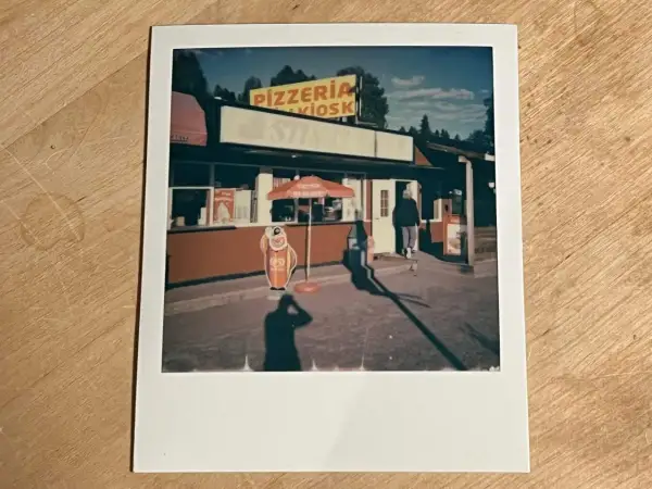 En polaroidkamera bild av en pizzeria och kiosk med en glasskylt. En person går in genom dörren.