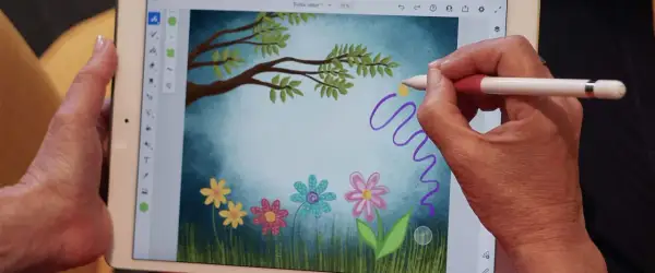 Handen skapar en magisk virvel med en penna i Adobe Fresco, över en bild av en drömsk äng med blommor och träd.